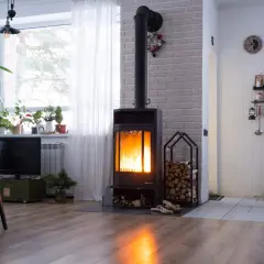 Palący się piec wolnostojący z czarnym kominem, obok stos drewna. Przepisy dotyczące podłączenia pieca do komina są kluczowe dla bezpieczeństwa.