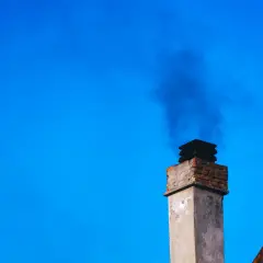 Dym z komina, być może dzięki zastosowaniu filtra kominowego zamiast wymiany pieca, unosi się na tle błękitnego nieba.