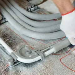 Ręce w białych rękawiczkach zaginają rury PEX za pomocą giętarki, przygotowując je do łączenia w posadzce.