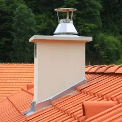 Nowy komin z nasadą, która pomoże jak wyeliminować ciąg wsteczny. Dachówki i las w tle.