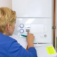 Kobieta sprawdza ustawienia pieca gazowego dwufunkcyjnego, który nie włącza się. Notuje coś na kartce.