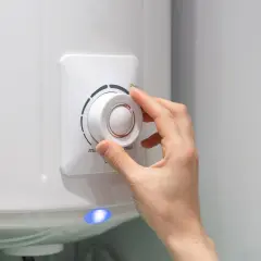 Dłoń reguluje termostat bojlera elektrycznego 50l, wpływając na to, ile prądu zużywa.