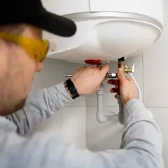 Instalator w okularach ochronnych podłącza bojler do instalacji CO.
