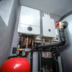 Dwa kotły gazowe z instalacją hydrauliczną, w tym czerwony zbiornik i rury odprowadzające skropliny z pieca gazowego.
