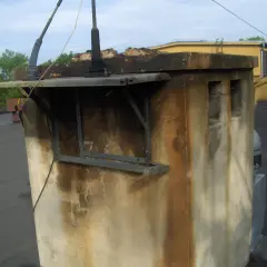 Brudny komin z widocznymi plamami, które sugerują nieprzyjemny smród. Na dachu widać też antenę i fragmenty budynków.