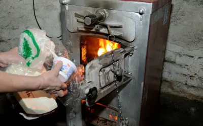 Ręce wkładają do pieca plastikowe opakowania i karton. Czy można palić kartonami w piecu? To pytanie budzi wątpliwości.