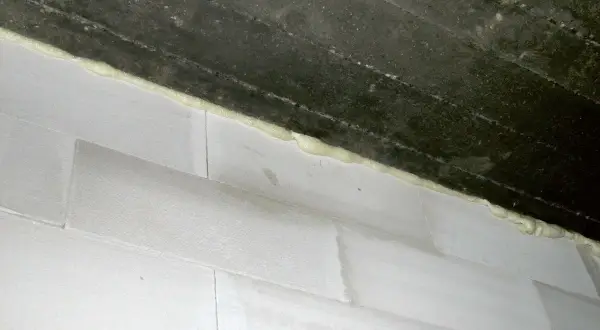 Dylatacja komina od stropu wykonana pianką montażową. Białe pustaki i ciemny strop.
