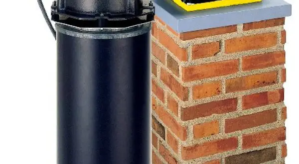 Nowoczesne zakończenie komina spalinowego z czarną obudową i wentylatorem, obok ceglanego komina.