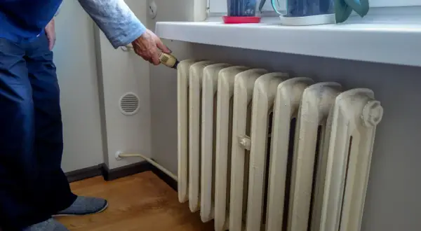 Mężczyzna reguluje termostat na grzejniku, szukając **ekonomicznego ogrzewania mieszkania w bloku**.
