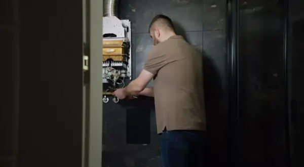 Mężczyzna naprawia piecyk gazowy Junkers, z którego kapie woda.