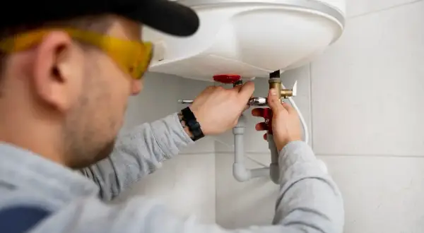 Instalator w okularach ochronnych podłącza bojler do instalacji CO.