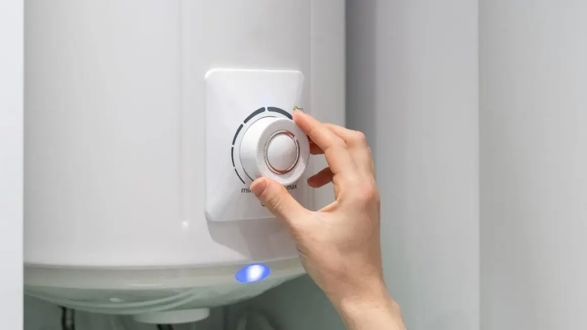 Dłoń reguluje termostat bojlera elektrycznego 50l, wpływając na to, ile prądu zużywa.
