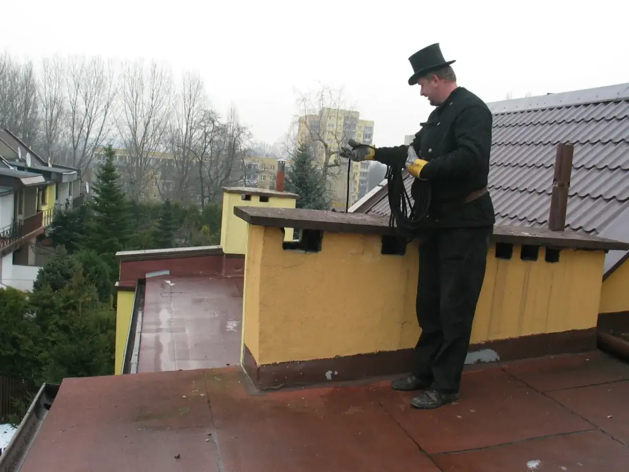 Kominiarz w cylindrze na dachu bloku, gotowy do czyszczenia przewodów kominowych.